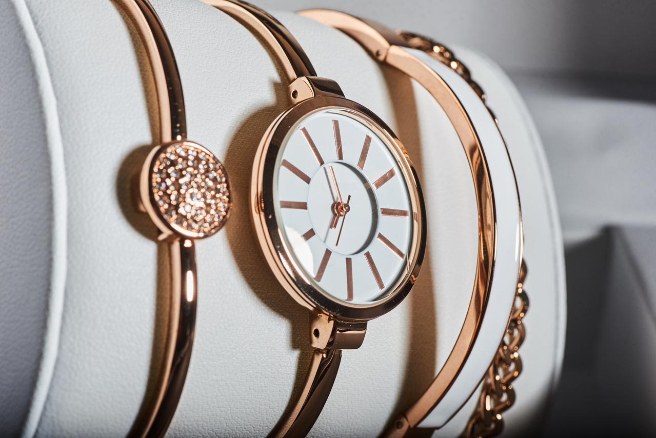 Reloj elegante con correa dorada y detalles en blanco, acompañado de pulseras modernas sobre un fondo de cuero blanco. Ideal para complementar cualquier atuendo.
